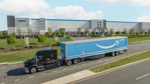 semi truck hauling amazon prime trailer past shipping facility