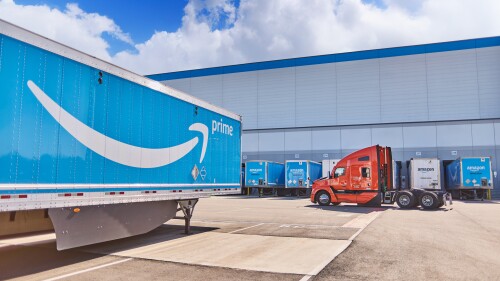 semi cab driving through a truck yard of Amazon Prime trailers
